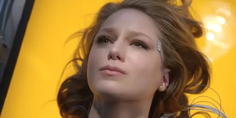Kara tumbada con electrodos en la sien bajo la luz amarilla de las lámparas solares del DEO, a punto de llorar