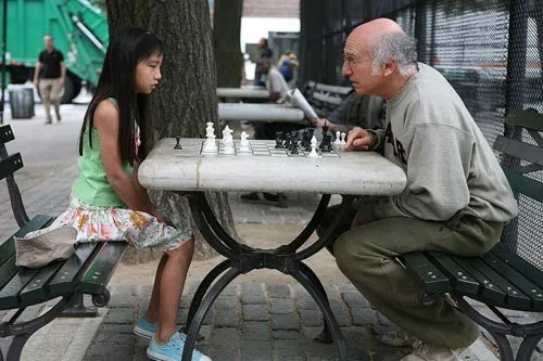 Larry David jugando al ajedrez con una niña en un parque en Si la cosa funciona