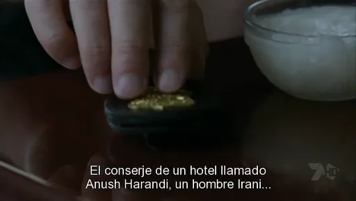 Unos dedos recogen un objeto dorado con un subtítulo sobre Anush Harandi en FlashForward