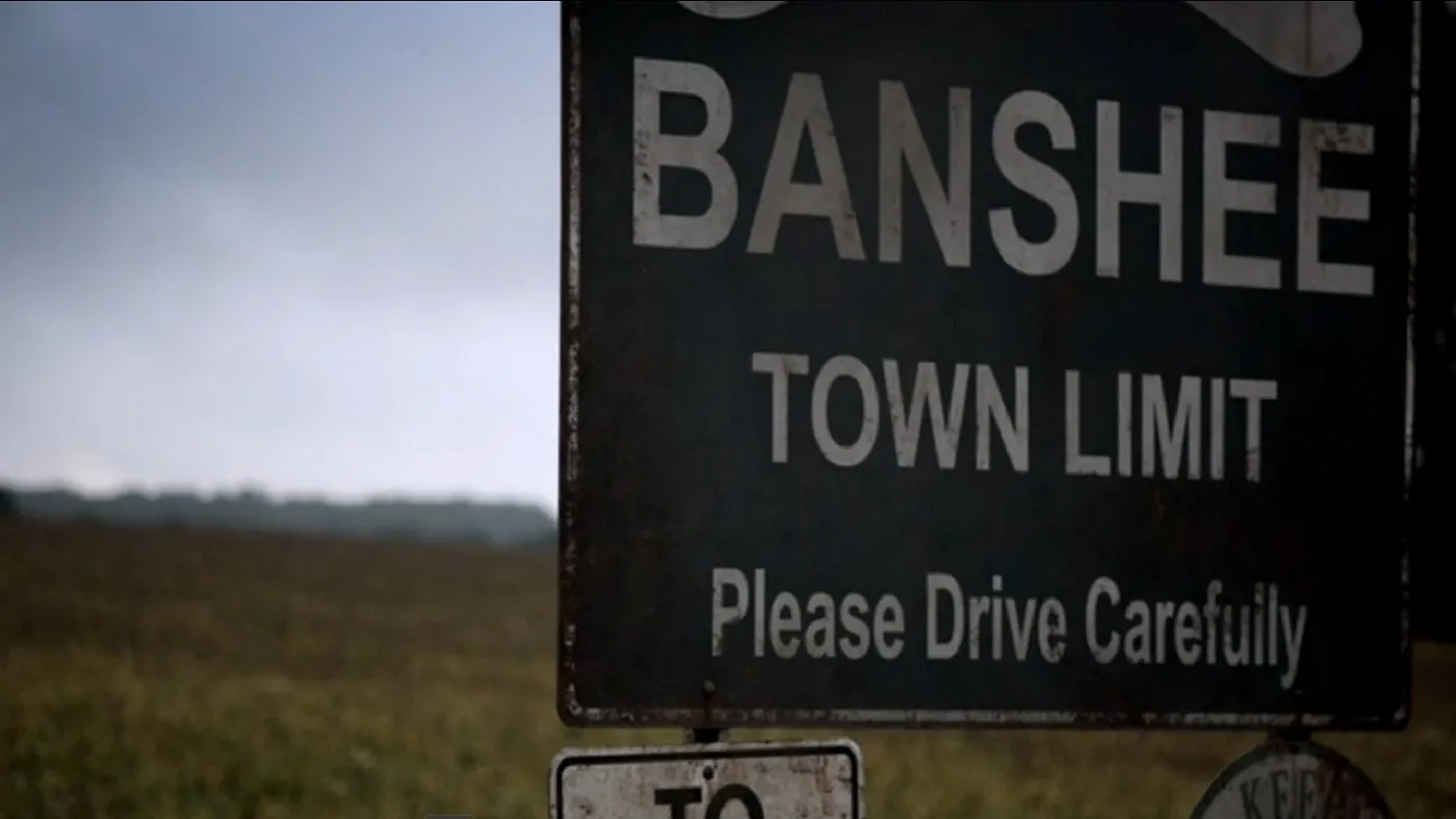 Cartel de «Banshee town limit, please drive carefully» bajo un cielo gris